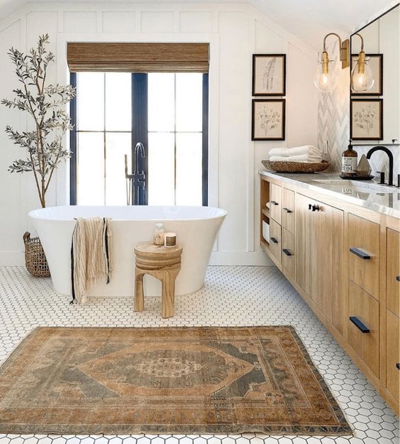 a modern farmhouse bathroom with paneled walls, a hex tile floor, a timber vanity, a tub, a mirror and shutters, wooden stools