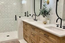 a modern farmhouse bathroom with printed and marble tile, a stained vanity, oval mirrors, black hardware and a boho rug