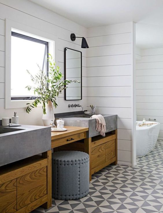 a modern farmhouse bathroom with shiplap walls, a geo tile floor, a stained timber vanity with concrete sinks, mirrors and black sconces