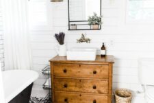 a modern farmhouse bathroom with white shiplap walls, a black printed tile floor, a vintage dresser vanity, a black tub and baskets