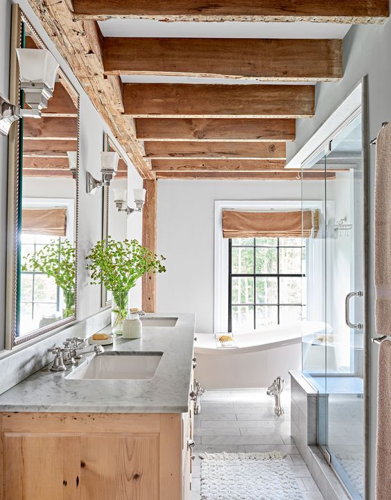 A modern farmhouse bathroom with wooden beams and a matching vanity, a shower space, a free standing tub and mirrors