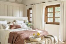 a modern farmhouse bedroom in neutrals, with a large wardrobe, a neutral bed with muted bedding, a woven bench and a printed rug