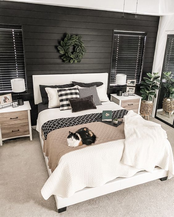 a modern farmhouse bedroom with a black shiplap wall, a white bed with contrasting bedding, stained nightstands , greenery