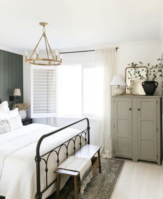 a modern farmhouse bedroom with a dark green accent wall, a wrought bed with neutral bedding, a grey storage unit and a bench