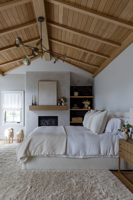 a modern farmhouse bedroom with a fireplace, a wooden ceiling, open shelves, a bed with neutral bedding, a fluffy rug