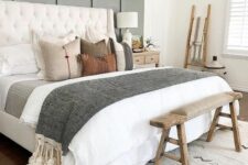a modern farmhouse bedroom with a grey paneled wall, a white upholstered bed with neutral bedding, a stained bench and a ladder
