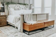 a modern farmhouse bedroom with a grey paneled wall, a wooden bed, stained nightstands, amber leather benches