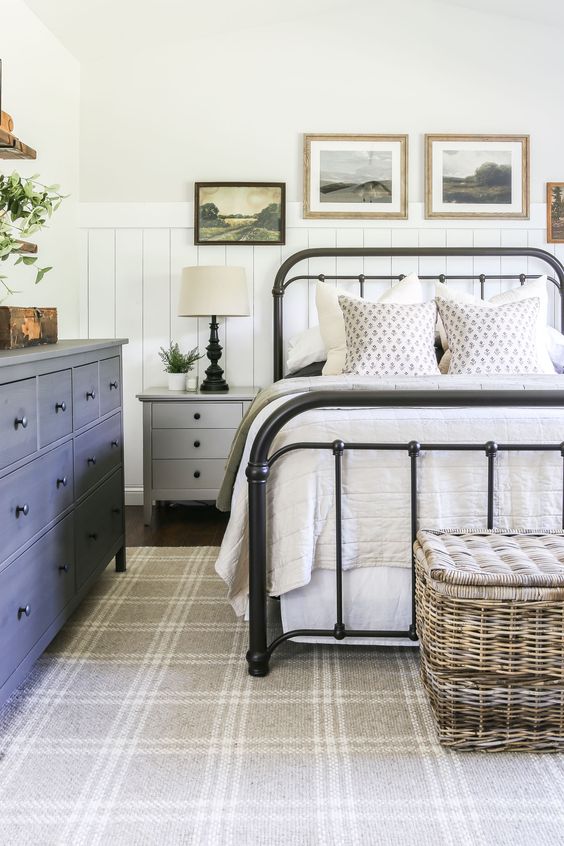 a modern farmhouse bedroom with shiplap, a blue IKEA Hemnes dresser, a wrought bed with neutral bedding, a grey nightstand, a basket chest and some artwork