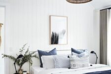 a modern farmhouse bedroom with shiplap walls, a white bed with navy and white bedding, stained stools and a woven pendant lamp