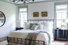a modern farmhouse bedroom with wooden beams, a wrought ceiling, black nightstands, neutral bedding and a chandelier