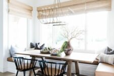 a modern farmhouse dining room with a built-in bench, a stained table, black chairs, a brass chandelier and pillows is cozy and cool
