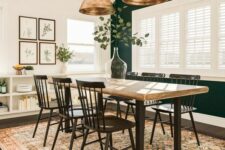 a modern farmhouse dining room with a forest green accent wall, a table with a wooden tabletop, black chairs, an IKEA storage unit and elegant brass pendant lamps