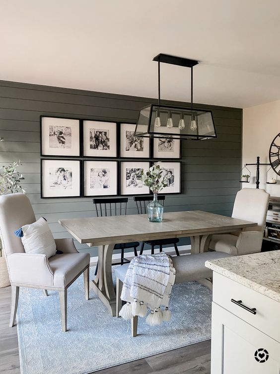 a modern farmhouse dining room with a green shiplap wall, a gallery wall, a stained table, grey seating furniture and a pendant lamp
