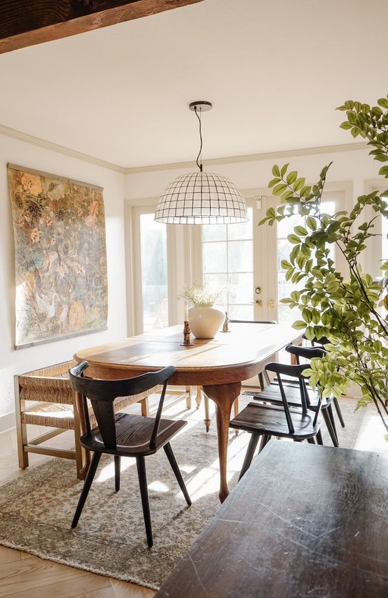 a modern farmhouse dining room with a rounded stained table, black chairs, a bench, a large scale artwork and a cool pendant lamp