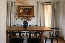 a modern farmhouse dining room with a stained table, black chairs, a woven pendant lamp and neutral textiles plus a lovely artwork