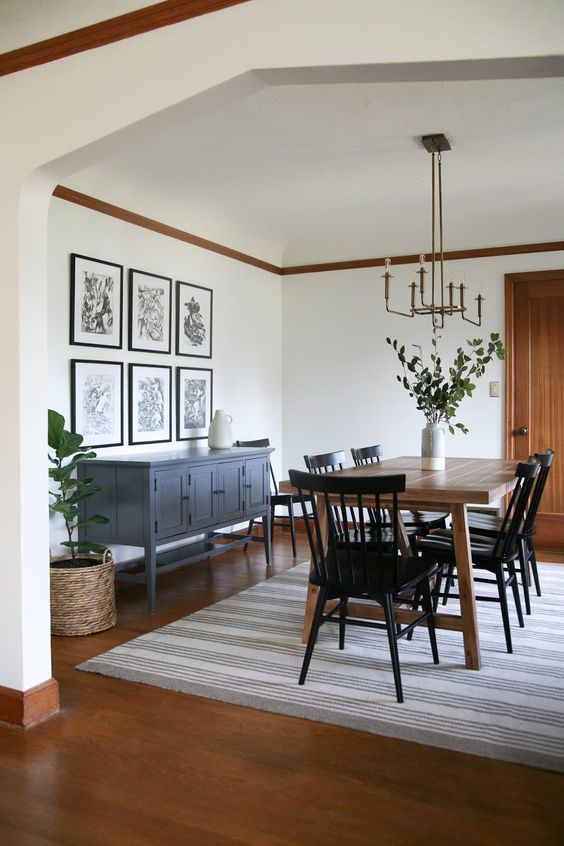 a modern farmhouse dining room with a vintage grey sideboard, a stained table and black chairs, a striped rug, a gallery wall