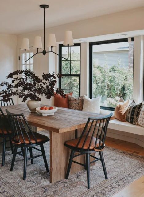 a modern farmhouse dining room with a windowsill seat and pillows, a stained table and black chairs and a potted plant
