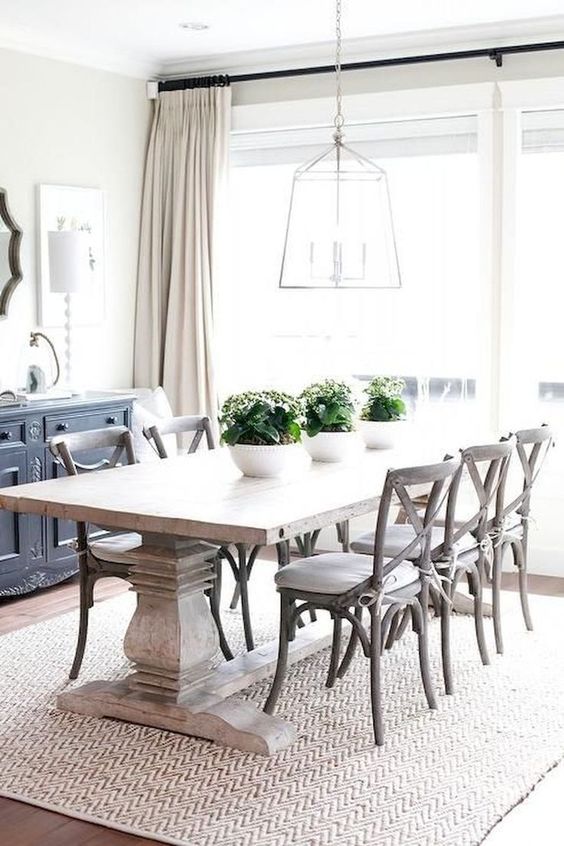 a modern farmhouse dining space with a black credenza, a heavy dining table, stained chairs, a pendant lamp and some potted greenery