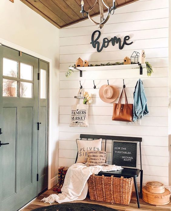 a modern farmhouse entry with a black bench, a basket, a shelf with some decor and greenery and some hooks