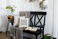 a modern farmhouse entryway with a black bench, a metal crate with greenery, a basket, a cotton wreath and some pillows
