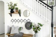 a modern farmhouse entryway with a rack with hooks, a stained bench with pillwos and a blanket, some greenery