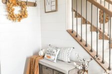 a modern farmhouse entryway with a storage bench, some amber bottles with cotton, a rack with a wreath and some decor on the walls