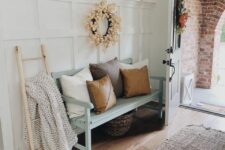 a modern farmhouse entryway with a white paneled wall, a mint bench with pillows and a blanket, a gallery wall and some pumpkins