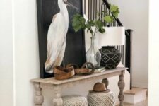 a modern farmhouse entryway with a whitewashed console table, woven poufs, some art and greenery is amazing