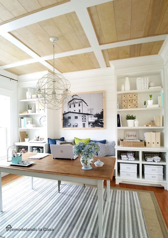 a modern farmhouse home office with a coffered ceiling, built-in bookcases, a desk, a bench with pillows and a sphere pendant lamp