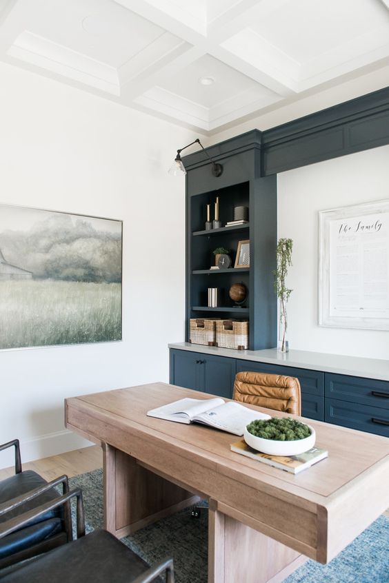 a modern farmhouse home office with a navy and white storage unit, a stained desk and leather chairs plus some greenery