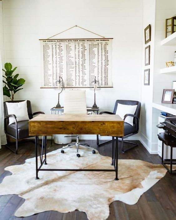 A modern farmhouse home office with a stained desk, black chairs, a built in storage unit and a cowhide rug