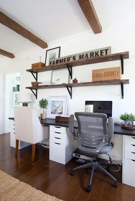 a modern farmhouse home office with an open shelving unit, a shared desk with a black countertop, some chairs and wooden beams