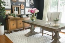 a modern farmhouse home office with black walls, a large and heavy desk, a creamy chair, a credenza, a gallery wall