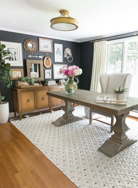 a modern farmhouse home office with black walls, a large and heavy desk, a creamy chair, a credenza, a gallery wall