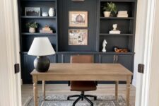 a modern farmhouse home office with graphite grey storage units, a stained desk, a brown chair, a boho rug and a table