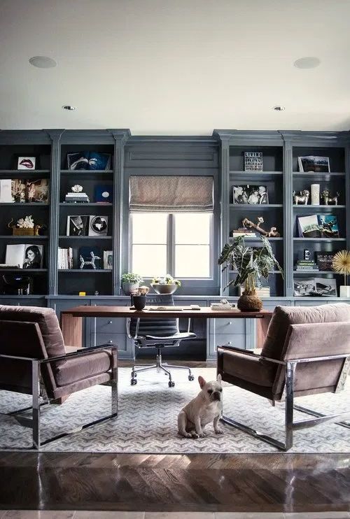 a modern farmhouse home office with grey storage units, a large desk, brown chairs, some plants and some decor