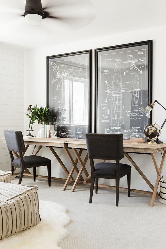 a modern farmhouse home office with trestle desks, large artwork, black chairs, striped poufs, greenery and some table lamps