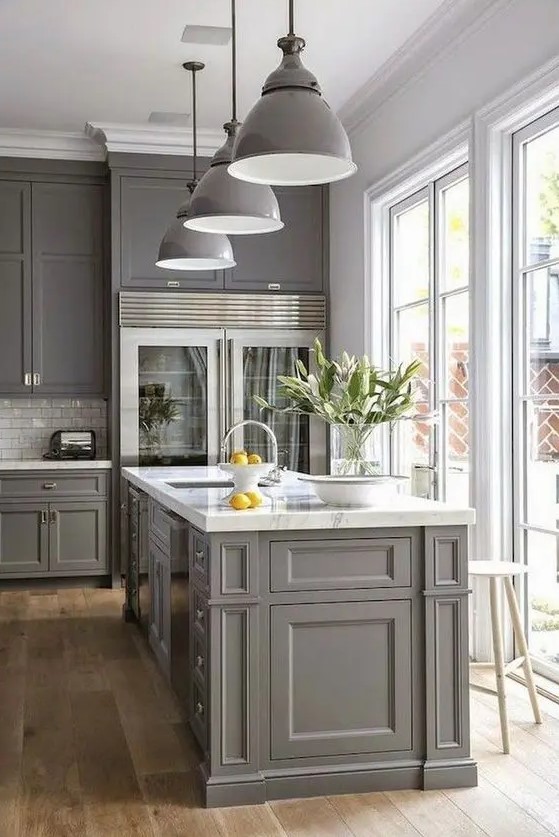 a modern farmhouse kitchen in grey with shaker style cabinets, a white subway tile backsplash, white marble countertops, grey pendant lamps