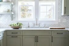 a modern farmhouse kitchen in sage green, with shaker cabinets, white stone countertops, white marble tiles and vintage fixtures