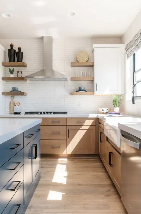 A modern farmhouse kitchen with light stained cabinets, a navy kitchen island, white stone countertops and a skinny tile backsplash, black handles