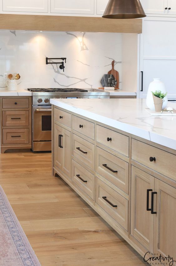a modern farmhouse kitchen with stained and white cabinets, white stone countertops and a backsplash, pendant lamps