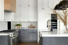 a modern farmhouse kitchen with white upper cabinets, dark grey lower ones, white countertops and a backsplash, black pendant lamps