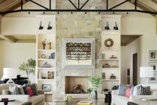 a modern farmhouse living room with a stone clad fireplace, neutral sofas, a dark leather daybed, coffee tables and a skylight