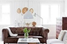 a modern farmhouse living room with white beadboard walls, vintage furniture and a brown leather Chesterfield
