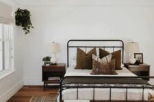 a modern farmhouse meets boho bedroom with a wrought bed and contrasting bedding, a stained bench, a printed rug, dark-stained nightstands and potted greenery