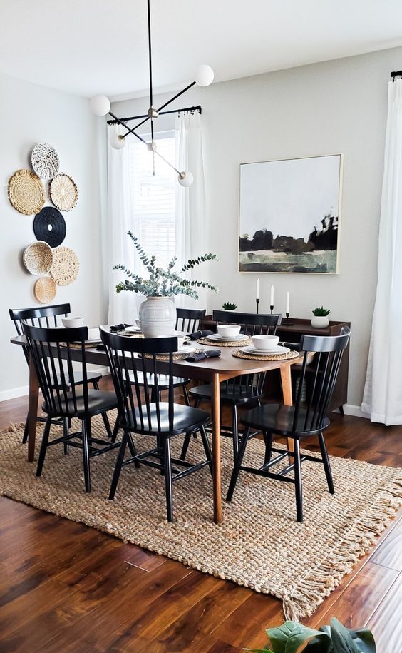 a modern farmhouse meets boho dining room with a stained table, a dark-stained credenza, black chairs, a gallery wall of plates and an artwork
