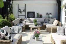 a modern farmhouse meets boho patio with wicker sofas, coffee tables, black and white pillows, candle lanterns and potted blooms