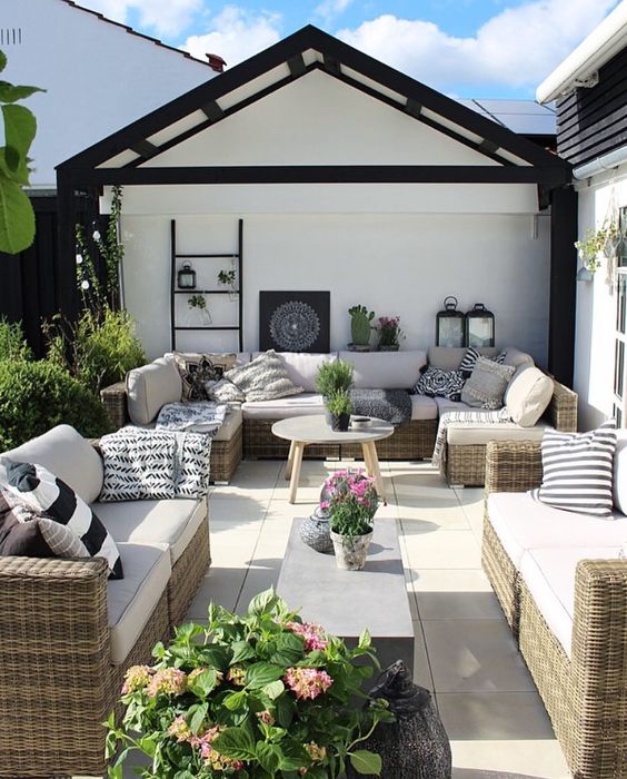 a modern farmhouse meets boho patio with wicker sofas, coffee tables, black and white pillows, candle lanterns and potted blooms