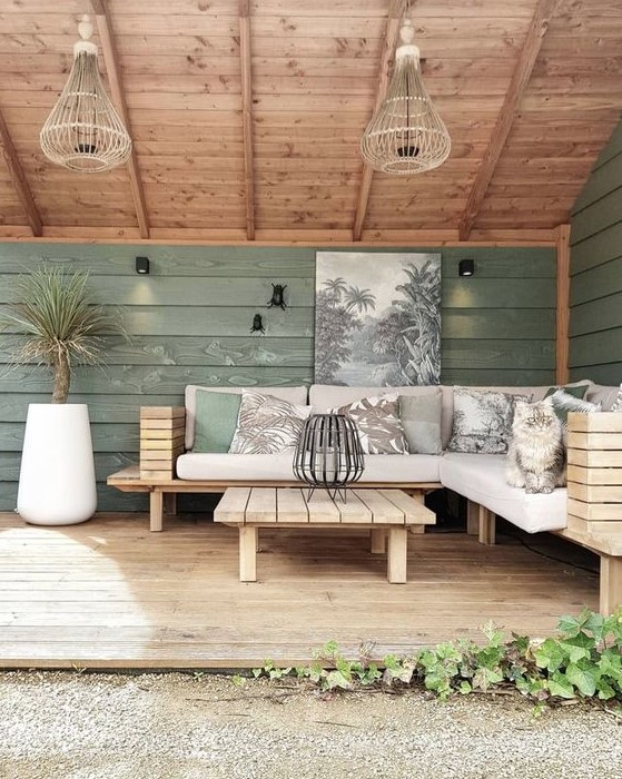 a modern farmhouse meets boho terrace with a large corner outdoor sofa, a matching table of wood slabs, potted plants and green walls