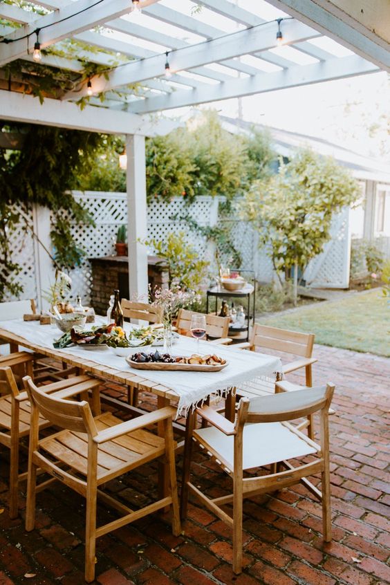 a modern farmhouse terrace with a fireplace, a stained dining set and some greenery around is a lovely dining space